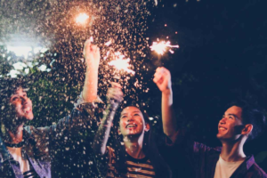 Three young adults laughing and holding sparklers at night, representing hope and a new normal after experiencing friendship breakups.