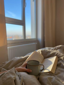 A person reading a book in a cozy, sunlit bedroom.